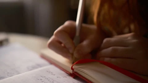 Student writing in notebook beside open textbooks, school materials 库存影片 341735857