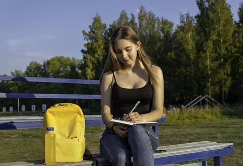 Student, writing in a notebook, in the park. Cute happy student girl sitting Stock Photos