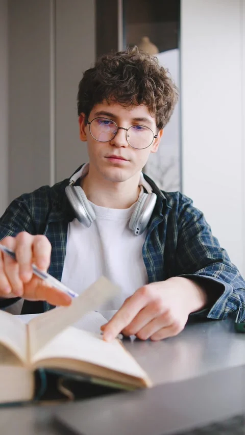 Student writing notes in a classroom setting while wearing headphones and Stock Footage 346186322