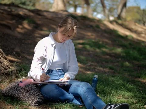 Student writing notes on her lap outdoors Stock Photos