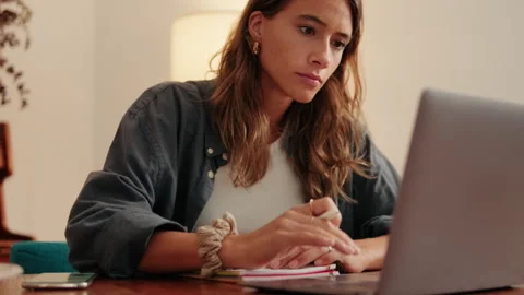 Student writing notes in a notebook looking at her laptop Stock Footage 297207020