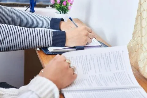 Student writing notes in notebook while another student reads at shared desk Stock Photos