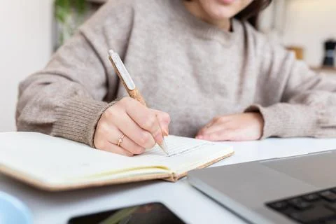 Student writing notes while learning on laptop at home Stock Photos