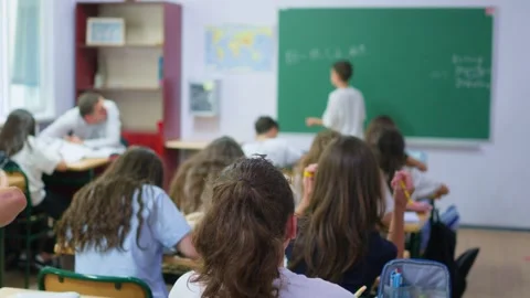 Students are sitting at their desks in the classroom, while a classmate is .. Stock Footage 345669176
