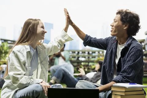 Students celebrating teamwork with high five on outdoor campus lawn Stock Photos