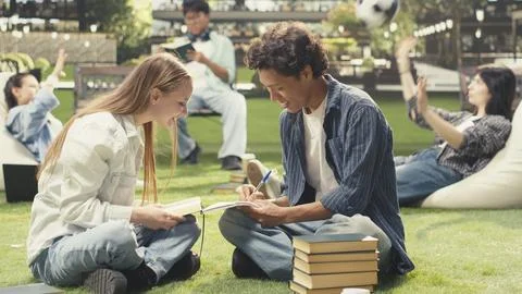 Students celebrating teamwork with high five on outdoor campus lawn Stock Photos