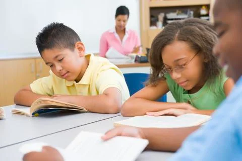 Students in class reading with teacher in background (selective focus) Stock Photos