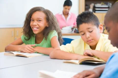 Students in class reading with teacher in background (selective focus) Stock Photos