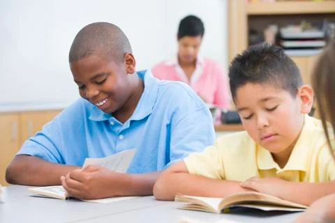 Students in class reading with teacher in background (selective focus) Stock Photos