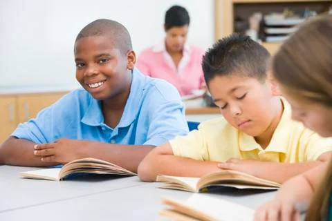 Students in class reading with teacher in background (selective focus) Stock Photos