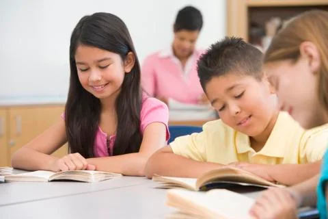 Students in class reading with teacher in background (selective focus) Stock Photos