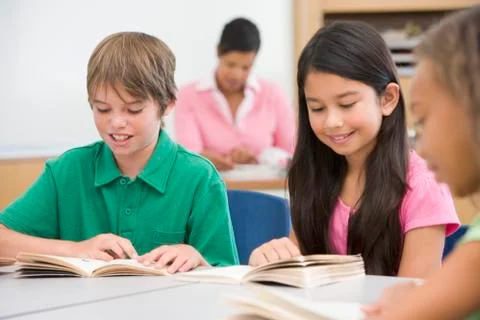 Students in class reading with teacher in background (selective focus) Stock Photos