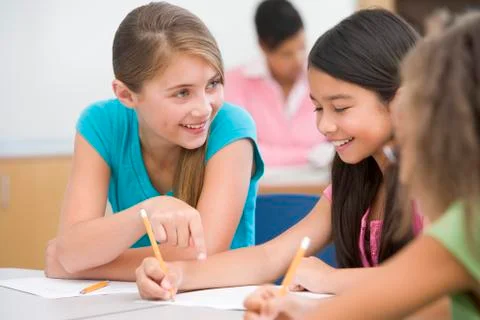 Students in class writing and talking with teacher in background (selective Stock Photos