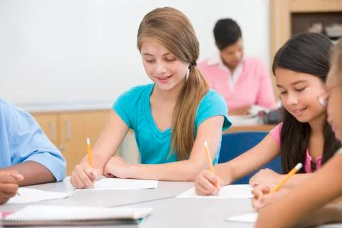 Students in class writing with teacher in background (selective focus) Stock Photos