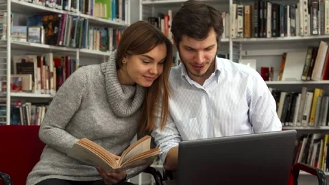 Students collaborate in the library, comparing a book with a laptop Video stock 311939656