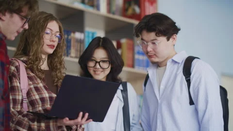 Students collaborating on laptop in library studying together with books and Stock Footage 341337530