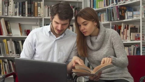 Students compare information in the book and on the laptop at the library Stock Footage 74283606