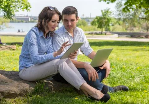 Students with electronic devises sitting on stone Stock Photos