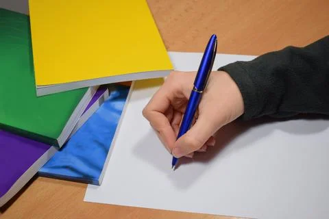 Students hand writing on blank white paper on the table with textbooks on the Фото
