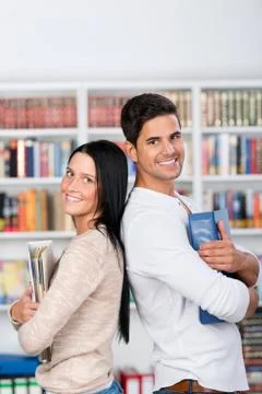 Students holding binders while standing back to back in library Stock Photos