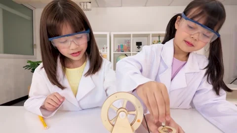 Students in Lab Coats Conducting Science Experiment with Wooden Wheel Stock Footage 340244383