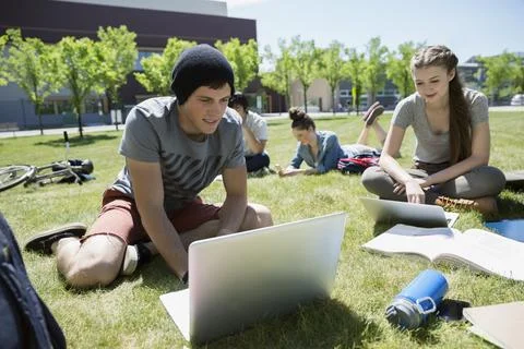 Students with laptops studying on sunny campus lawn Stock Photos