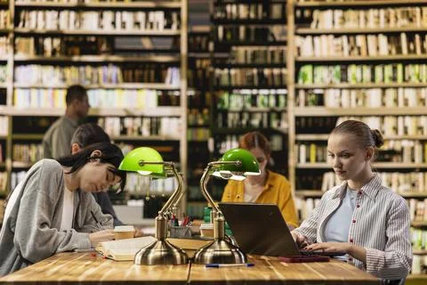 Students learning together at long library table with laptop and open books Stock Photos