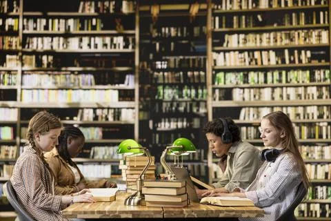 Students learning together at shared wooden desk with open books Stock Photos
