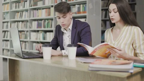 Students in a library at school use computer and book and talk for projects Stock Footage 131101077