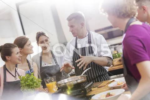 Students listening to chef teacher in cooking class kitchen Stock Photos