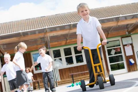 Students playing outdoors during recess one with a tricycle scooter (selective Stock Photos
