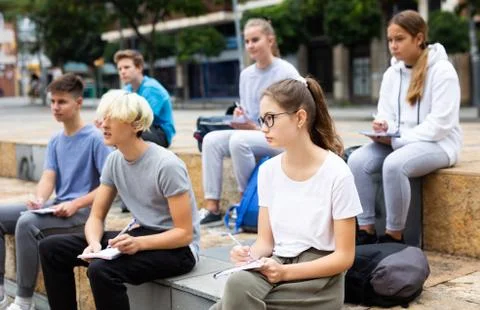 Students record lecture while sitting on a stone street parapet Stock Photos