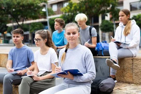 Students record lecture while sitting on a stone street parapet Stock Photos