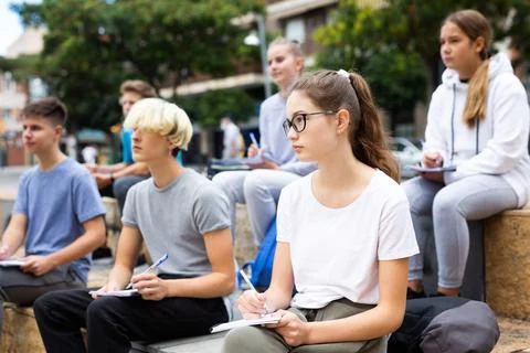 Students record lecture while sitting on a stone street parapet Foto stock