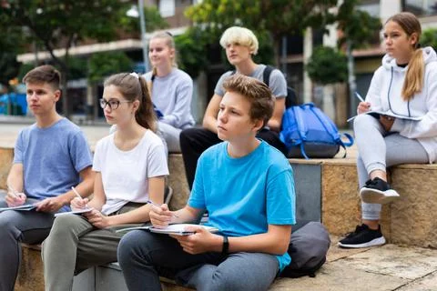 Students record lecture while sitting on a stone street parapet 写真素材