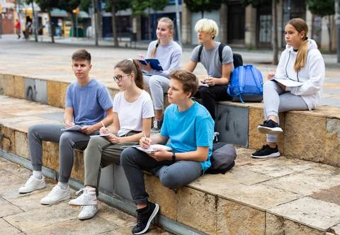 Students record lecture while sitting on a stone street parapet 스톡 사진