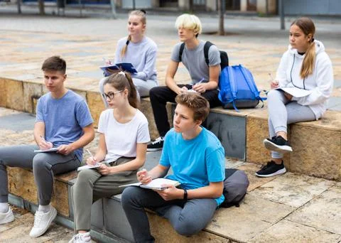 Students record lecture while sitting on a stone street parapet Foto stock