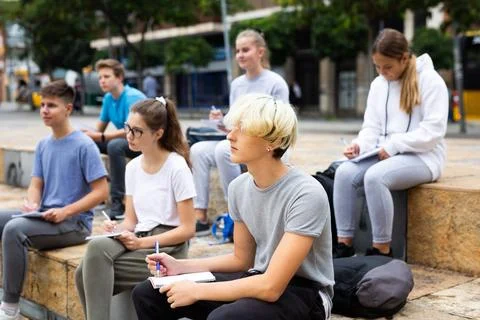 Students record lecture while sitting on a stone street parapet Foto stock