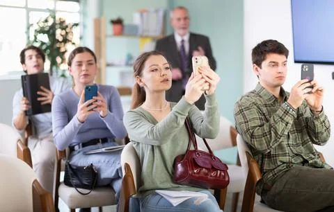 Students scanning QR code or taking photo, professor in background Foto stock