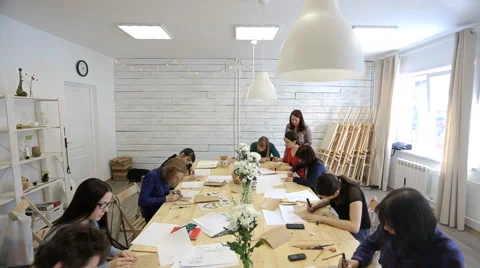 Students sit around long squared wooden table and draw sketches 库存影片 64956340