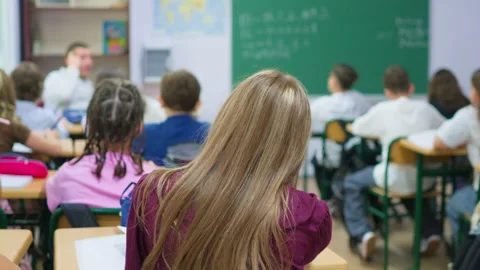 Students sitting at desks in a classroom raising hands to participate in a .. Stock Footage 345669171