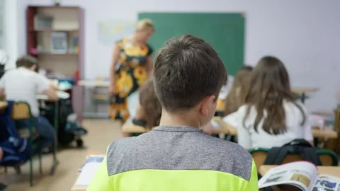 Students sitting at desks in a classroom with a teacher standing in front o.. Stock Footage 346181491