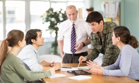 Students solving issues at the table in front of the teacher Stock Photos