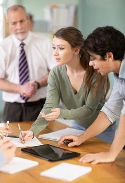 Students solving issues at the table in front of the teacher Stock Photos
