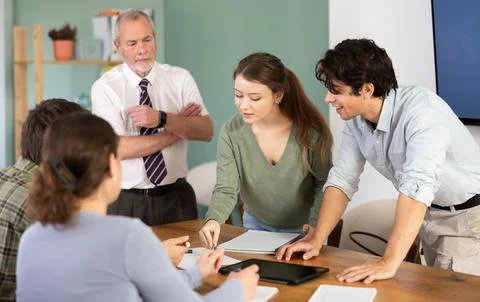Students solving problems at table with teacher in background Foto stock