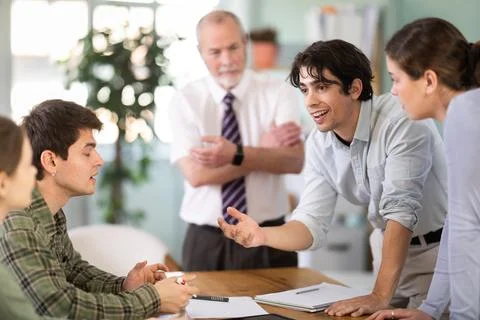 Students solving problems at table with teacher in background Foto stock