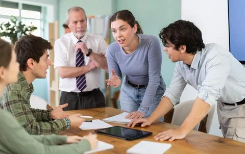 Students solving problems at table with teacher in background Stock Photos