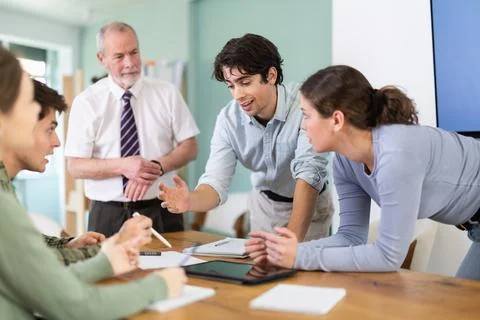 Students solving problems at table with teacher in background Stock Photos