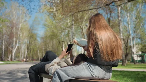Students study and laugh on bench with book and phone, caucasian and asian Stock Footage 329473924