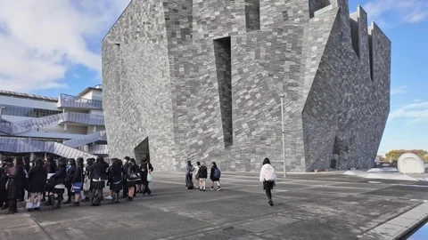 Students in uniform walk past a modern concrete building on campus. Vídeos de archivo 346012063